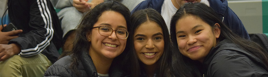 Three students smiling, sitting in the bleachers