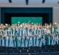 Seniors wearing green and white caps and gowns, waving hands and showing scholarship awards